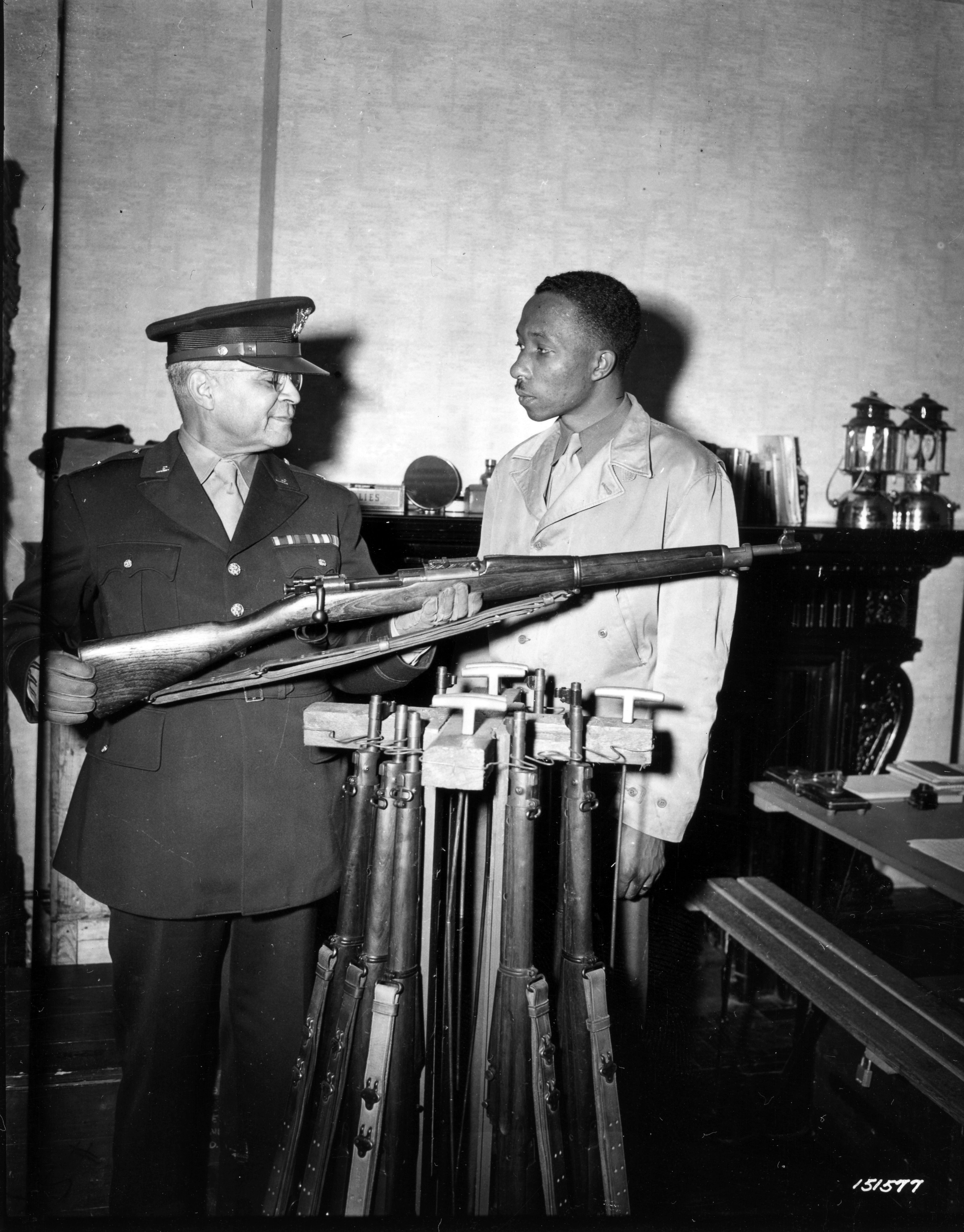 Historical image showing Brig. General Benjamin O. Davis explains mechanics of a rifle to a Black trooper. of Black American soldiers during WWII