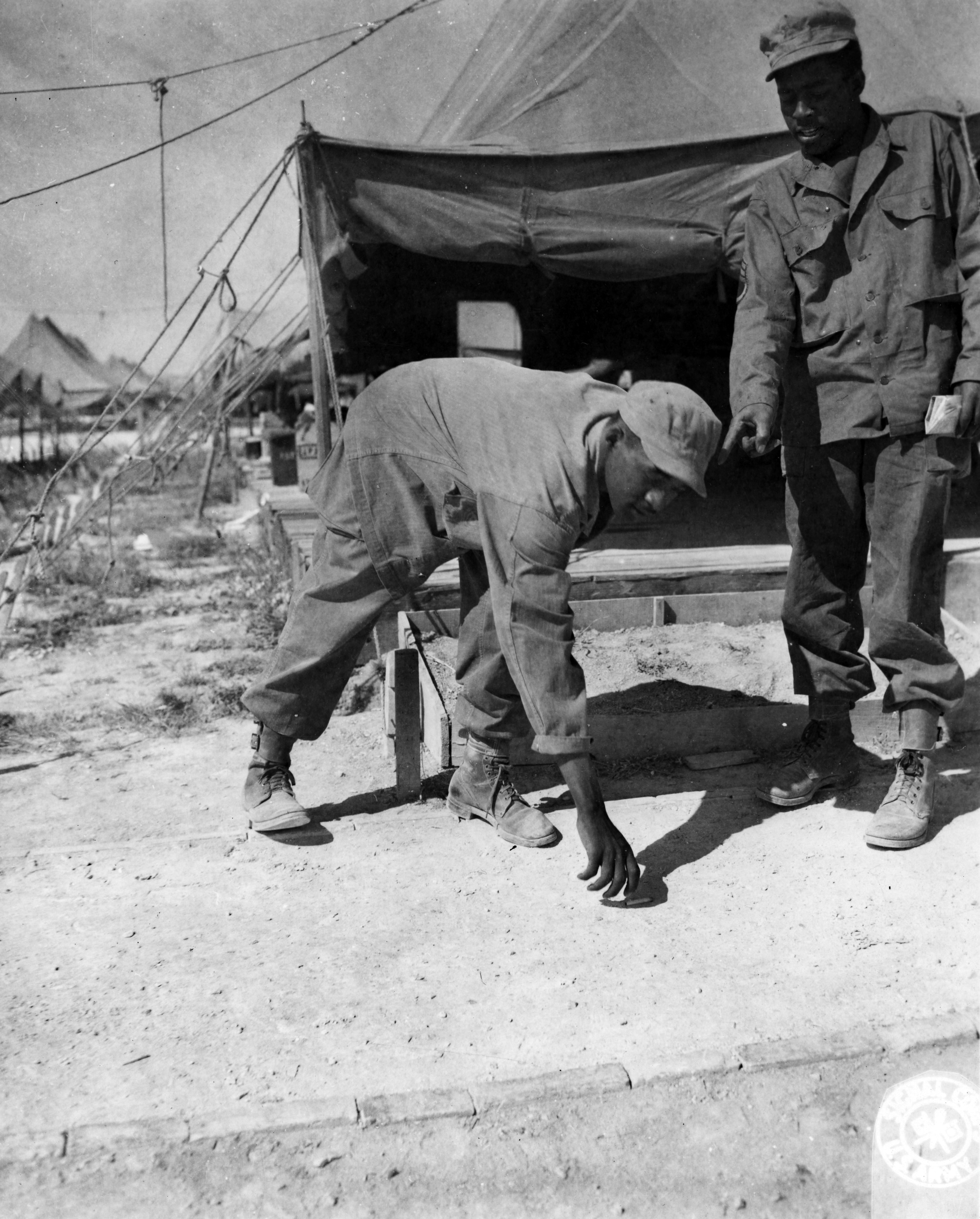 Historical image showing S/Sgt. Jacobs E. White, RT 4 Sumter, S.C., pulls his rank on his twin brother, Corporal Benjamin S. White, by getting him to police up the area at Camp Atlanta near Chalons, France. of Black American soldiers during WWII