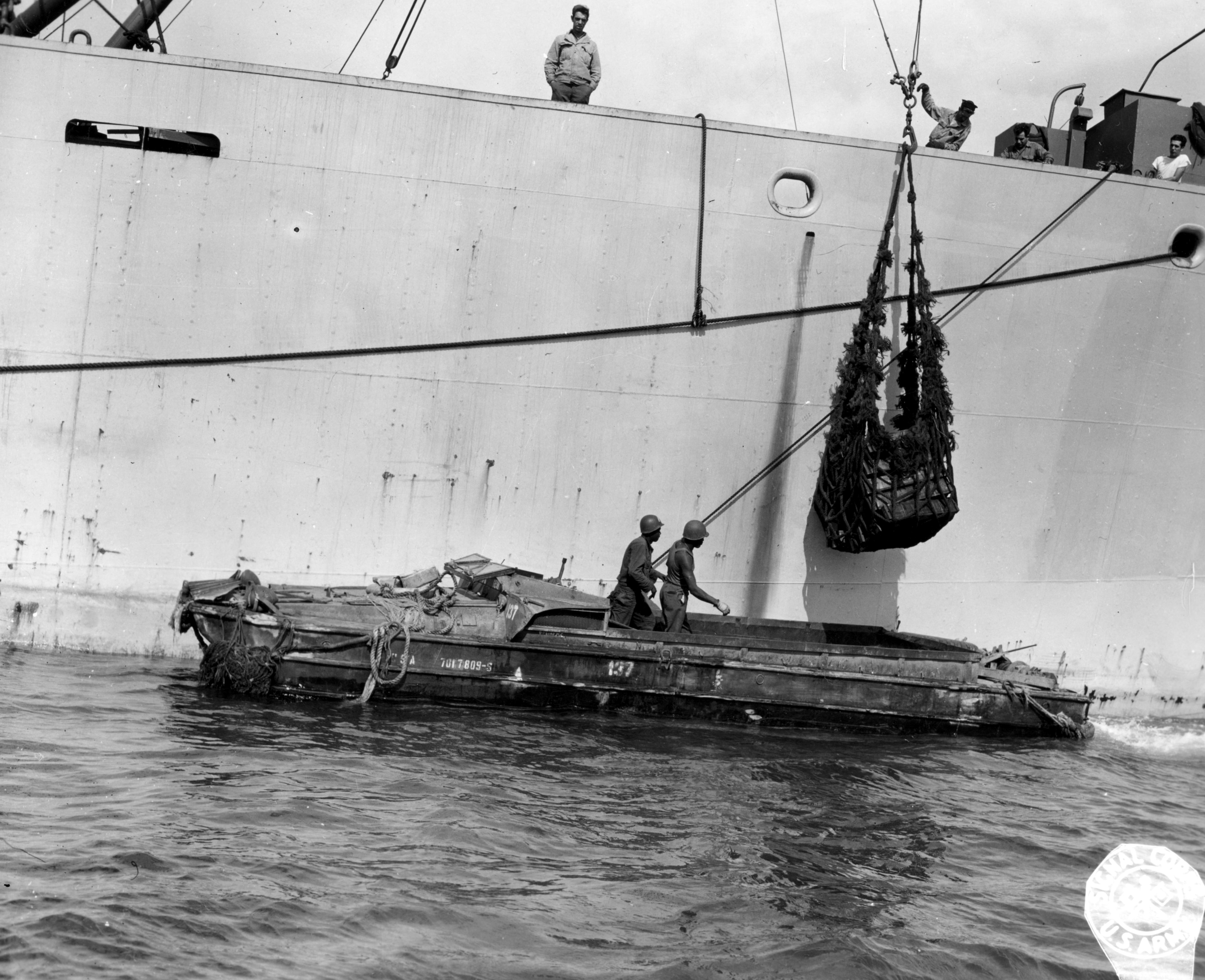 Historical image showing Private Alfred Roberts and Private Louis Peters transfer ammunition from a Liberty ship to the coast of France using a DUKW. of Black American soldiers during WWII