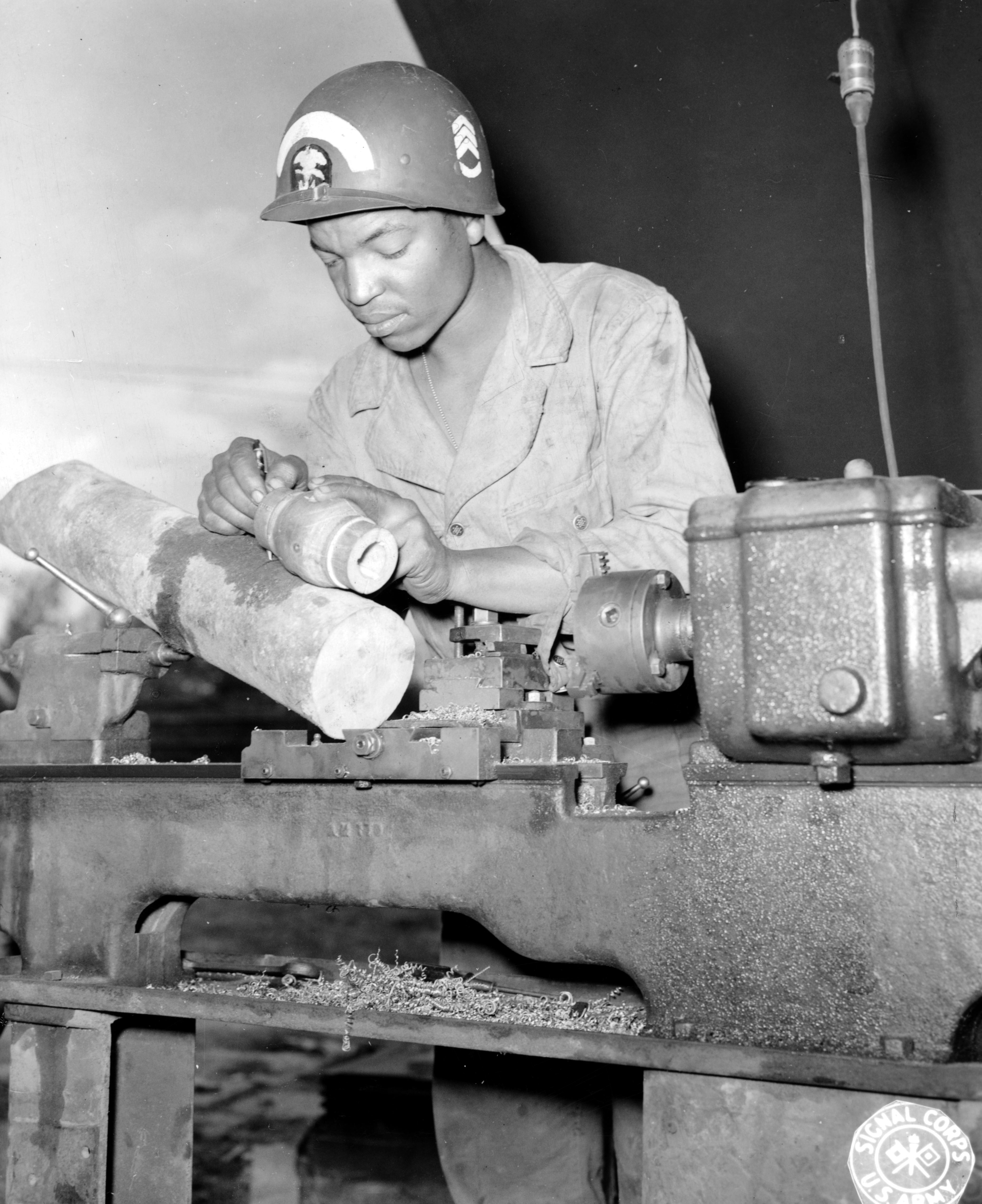 Historical image showing S/Sgt. Sam Beal makes a wooden stud bearing for a DUKW. of Black American soldiers during WWII