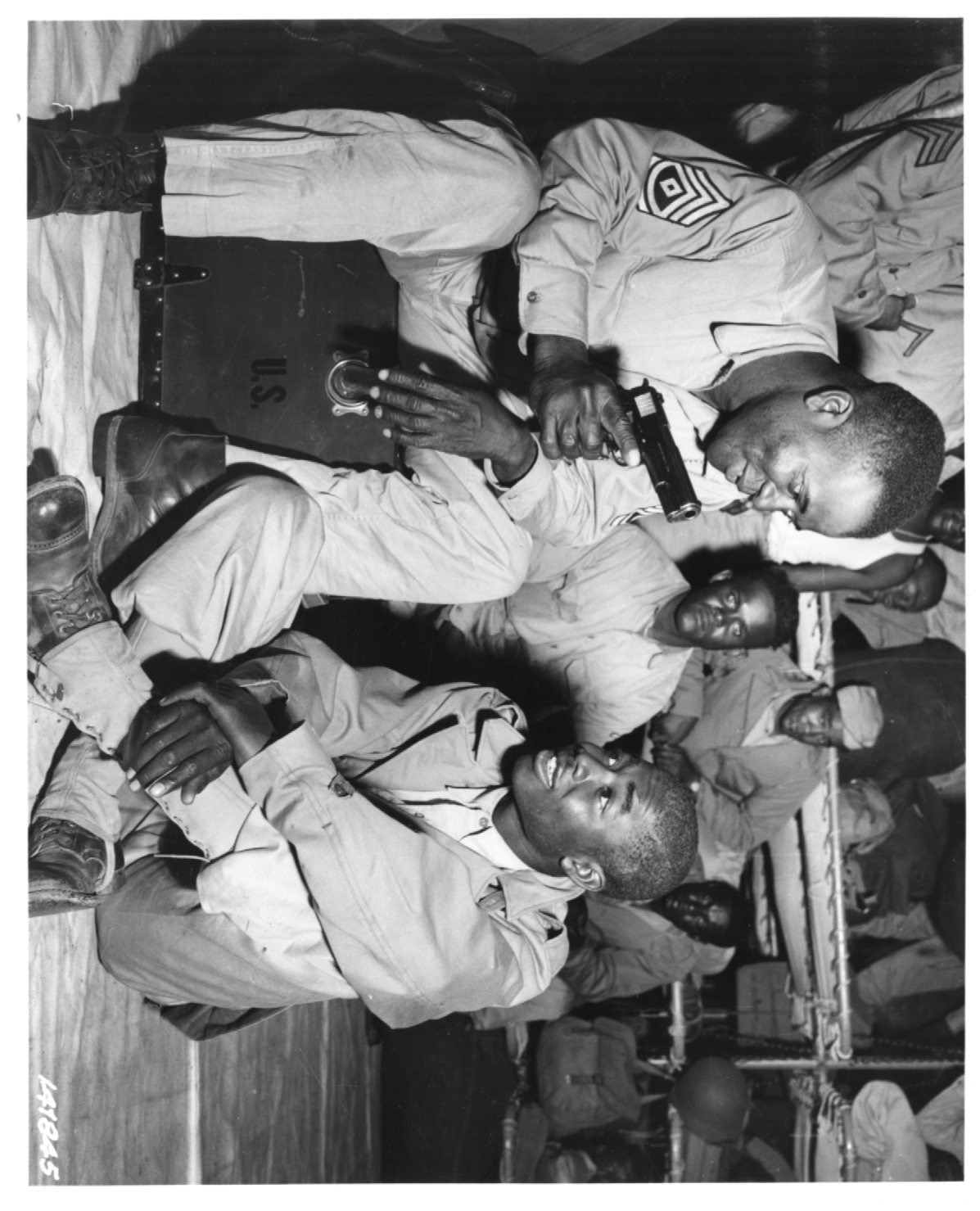 Historical image showing First Sergeant James Sims shows Private John Stephens his .45 pistol of Black American soldiers during WWII