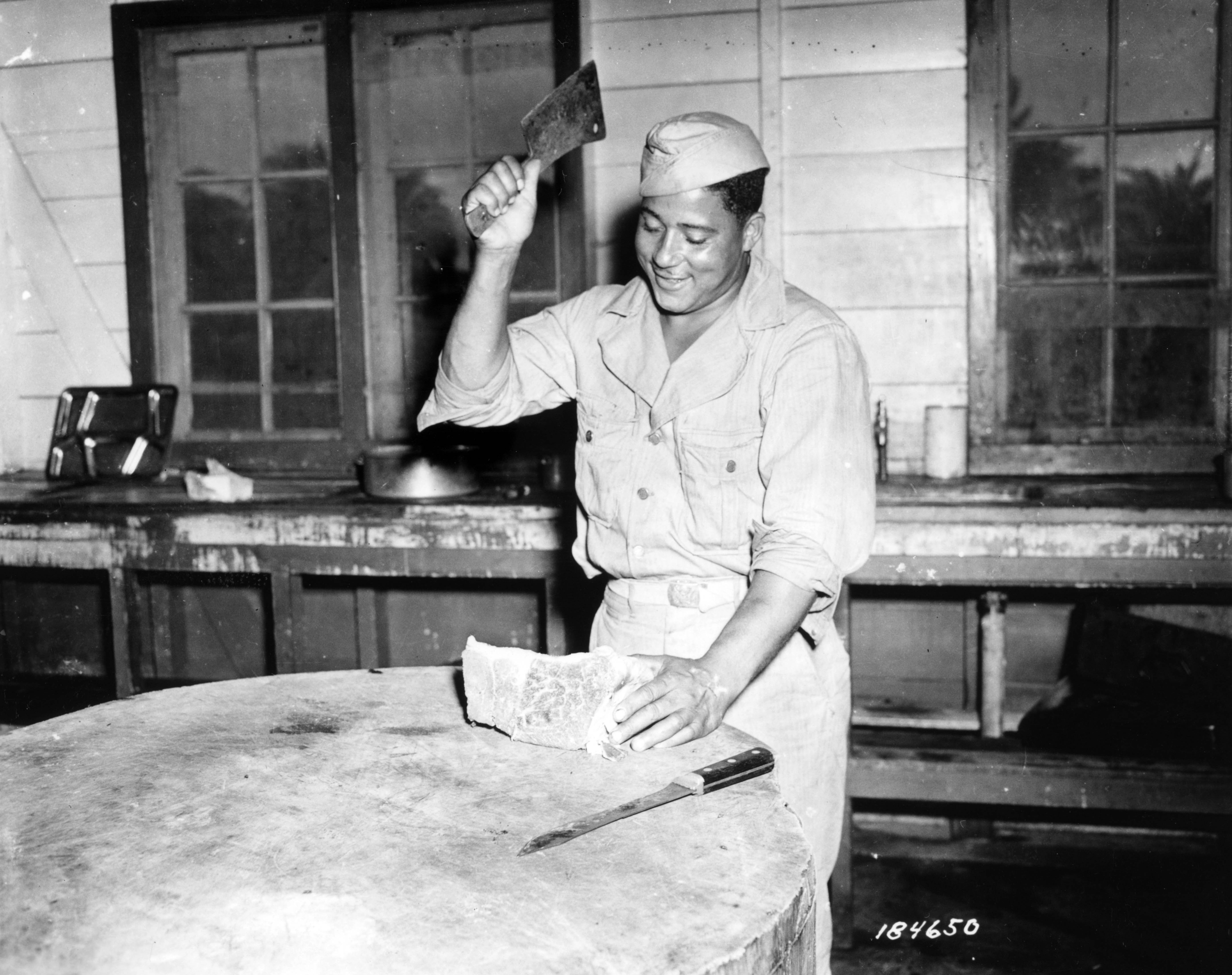 Historical image showing A good dinner is in store for a company of an Air Base Security Battalion in the South Pacific Area, judging by the smile of Sgt. Walter Rothschild. of Black American soldiers during WWII