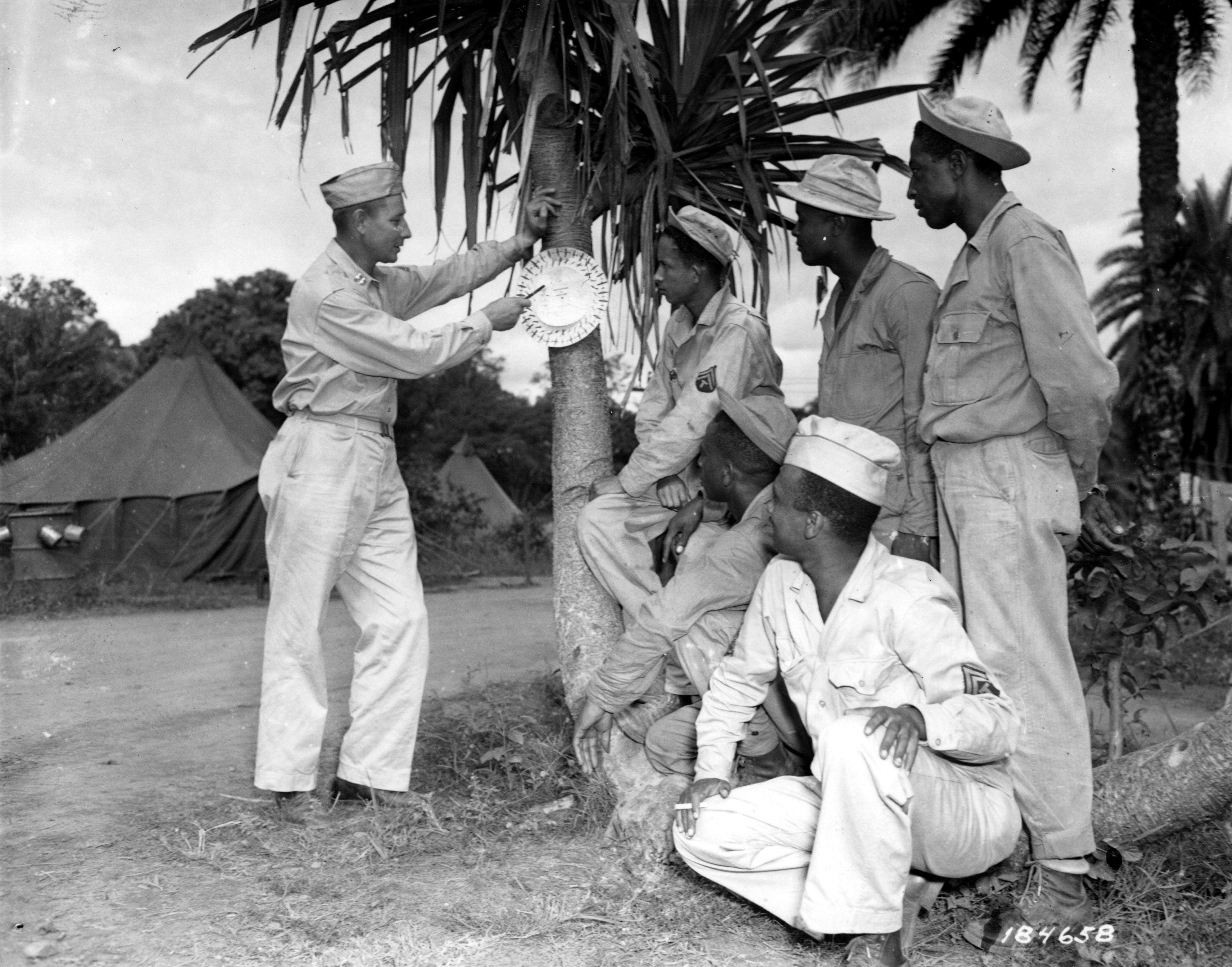 Historical image showing An outdoor class in airplane identification is held by Capt. Seymour Tucker of an Air Base Security Battalion. of Black American soldiers during WWII
