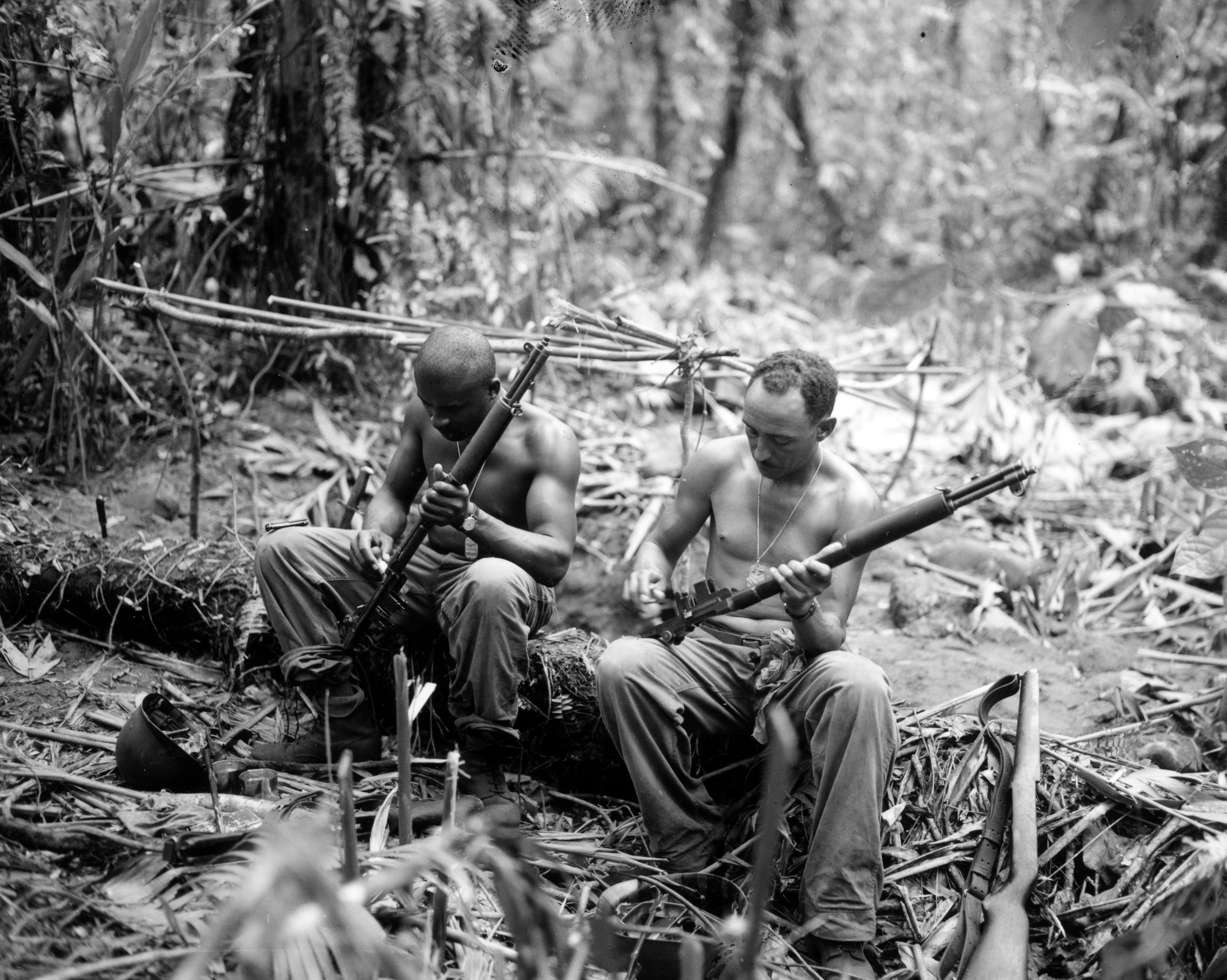 Historical image showing Sgt. John C. Clark, Lorman, Miss., and S/Sgt. Ford M. Shaw, Tuscon, Arizo., (l-r) clean their rifles in bivouac area alongside the (illegible) Trail, Bogainville. of Black American soldiers during WWII
