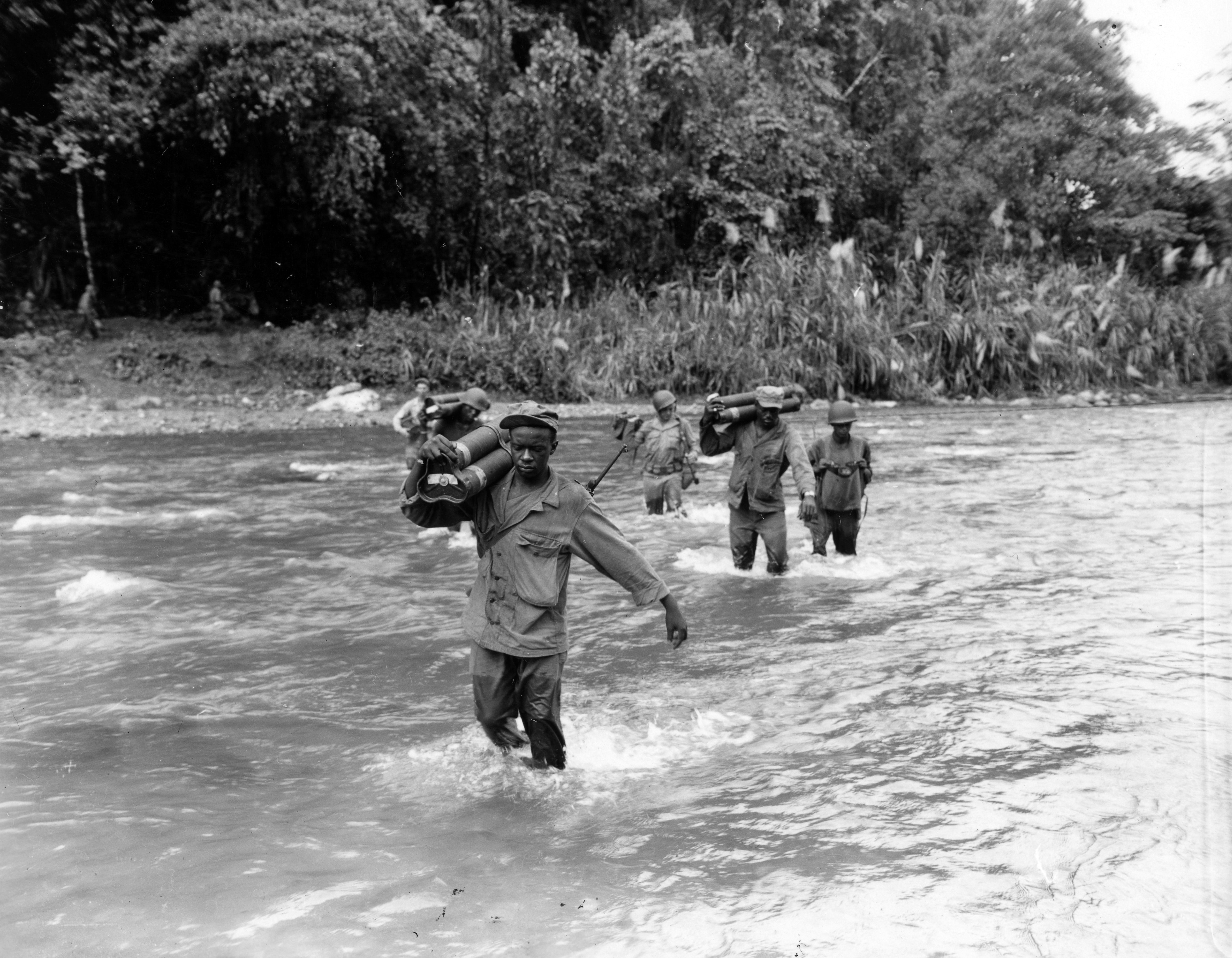 Historical image showing Members of the 2nd Bn., 25th Combat Team, 93rd Div., wade across the Laruma River carrying mortar shells to the other side. of Black American soldiers during WWII