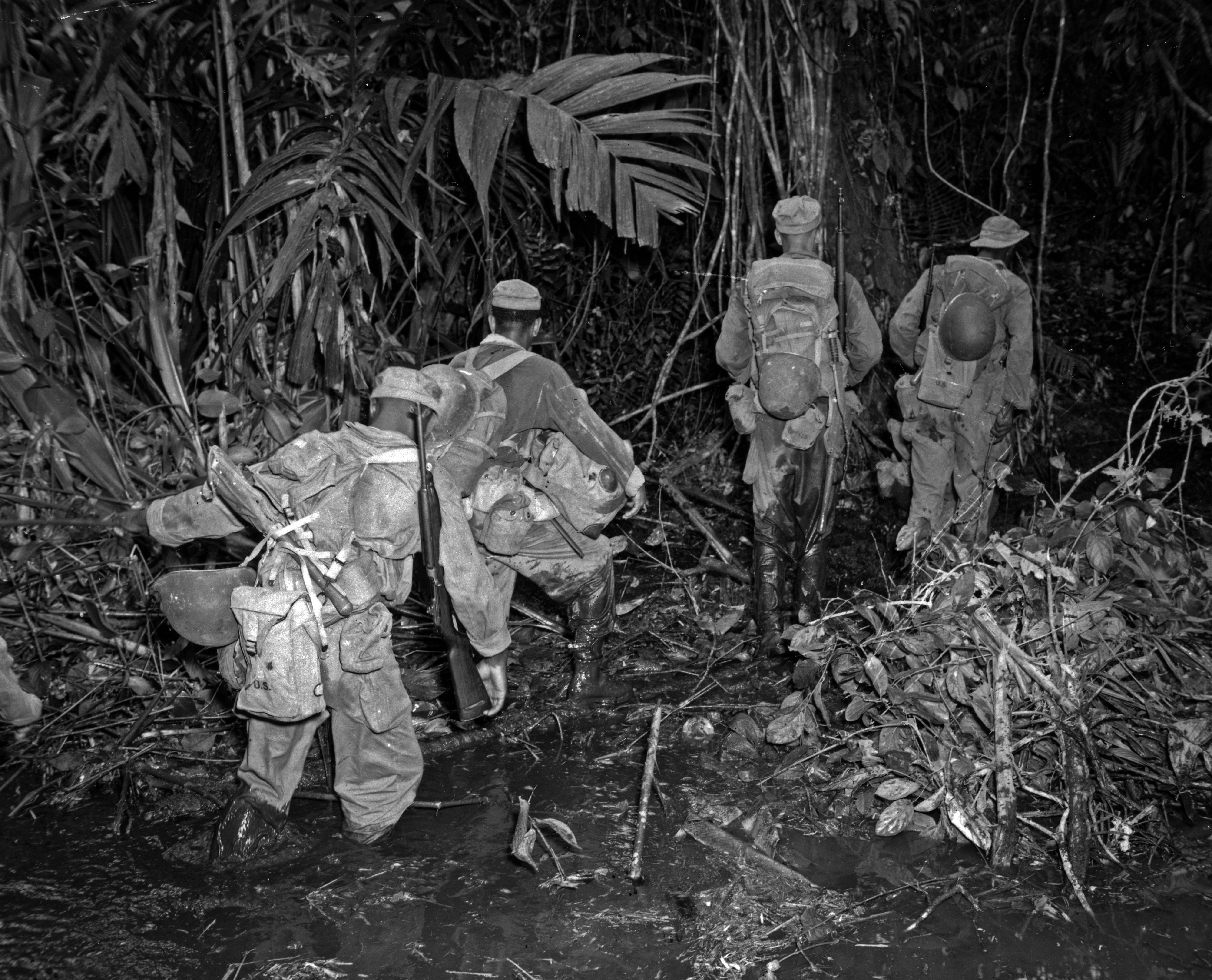 Historical image showing En route to Hill 165, members of the 93rd Division struggle through clinging mud along the East-West trail on an island in the South Pacific. of Black American soldiers during WWII