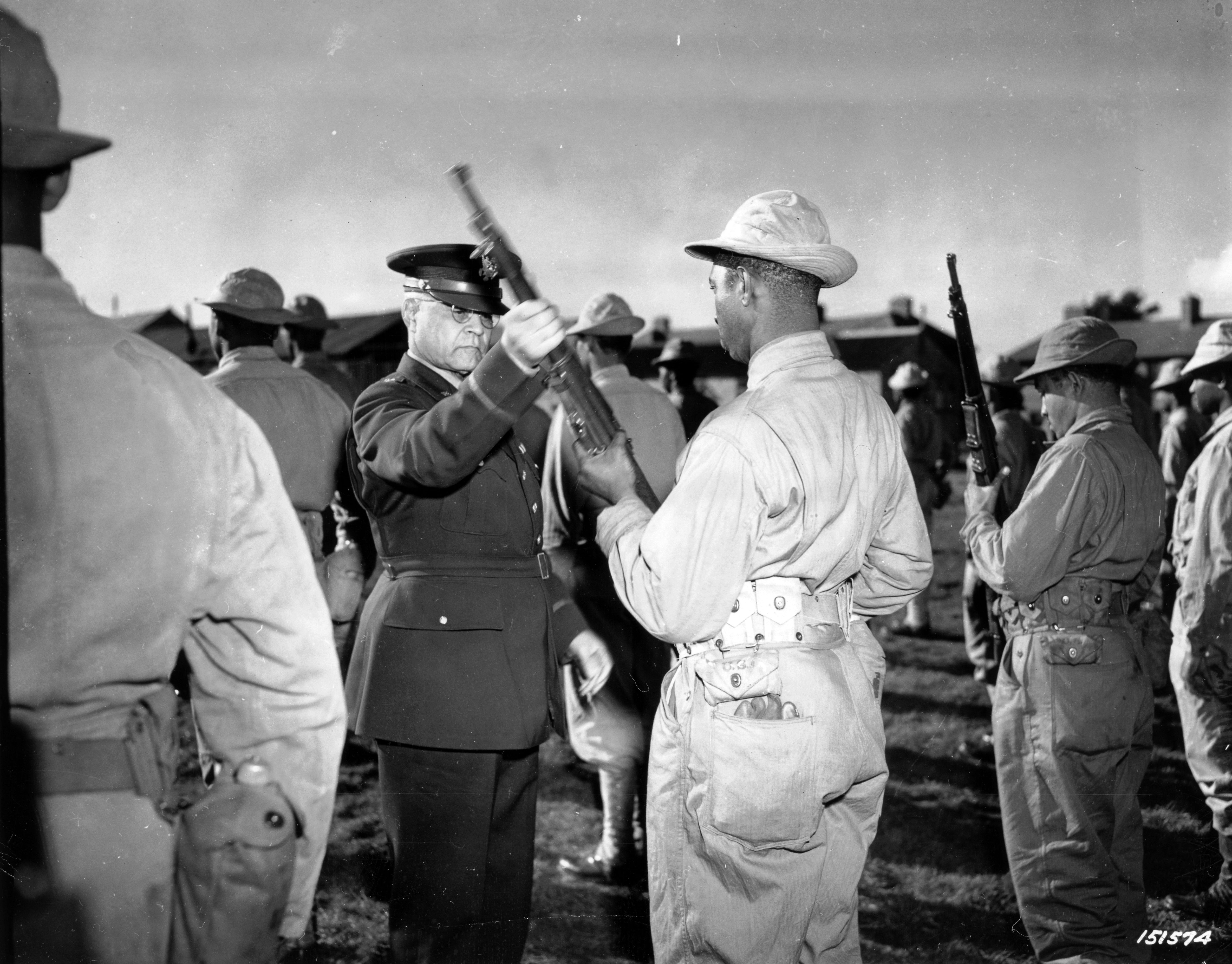 Historical image showing During an inspection tour of Black troops of the Services of Supply somewhere in England, Brigadier General Benjamin O. Davis examines a rifle of one of the men. of Black American soldiers during WWII