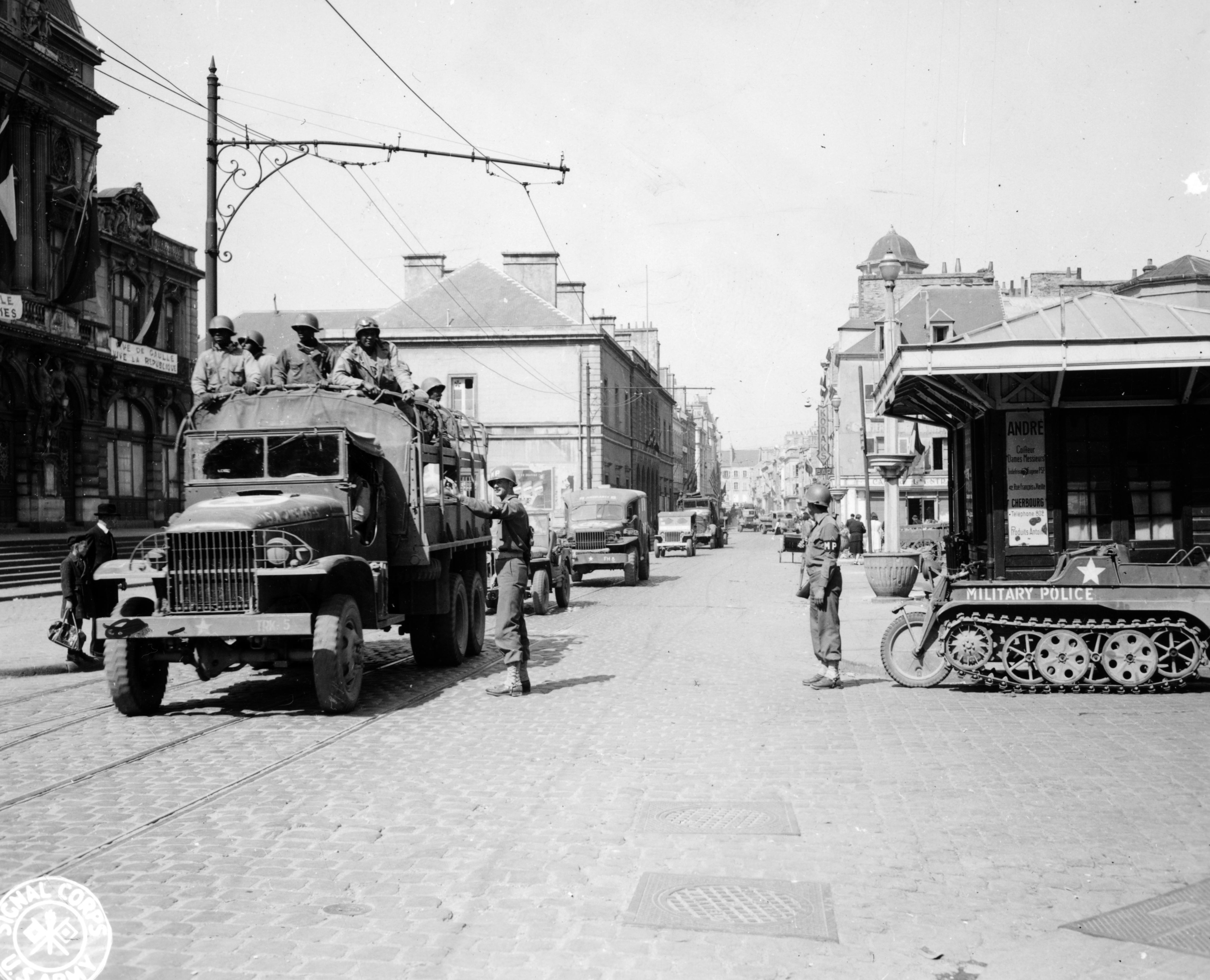 Historical image showing Private First Class Albert Buhlig and Private First Class Pedro Hernandez direct traffic through the streets of Cherbourg, France. of Black American soldiers during WWII