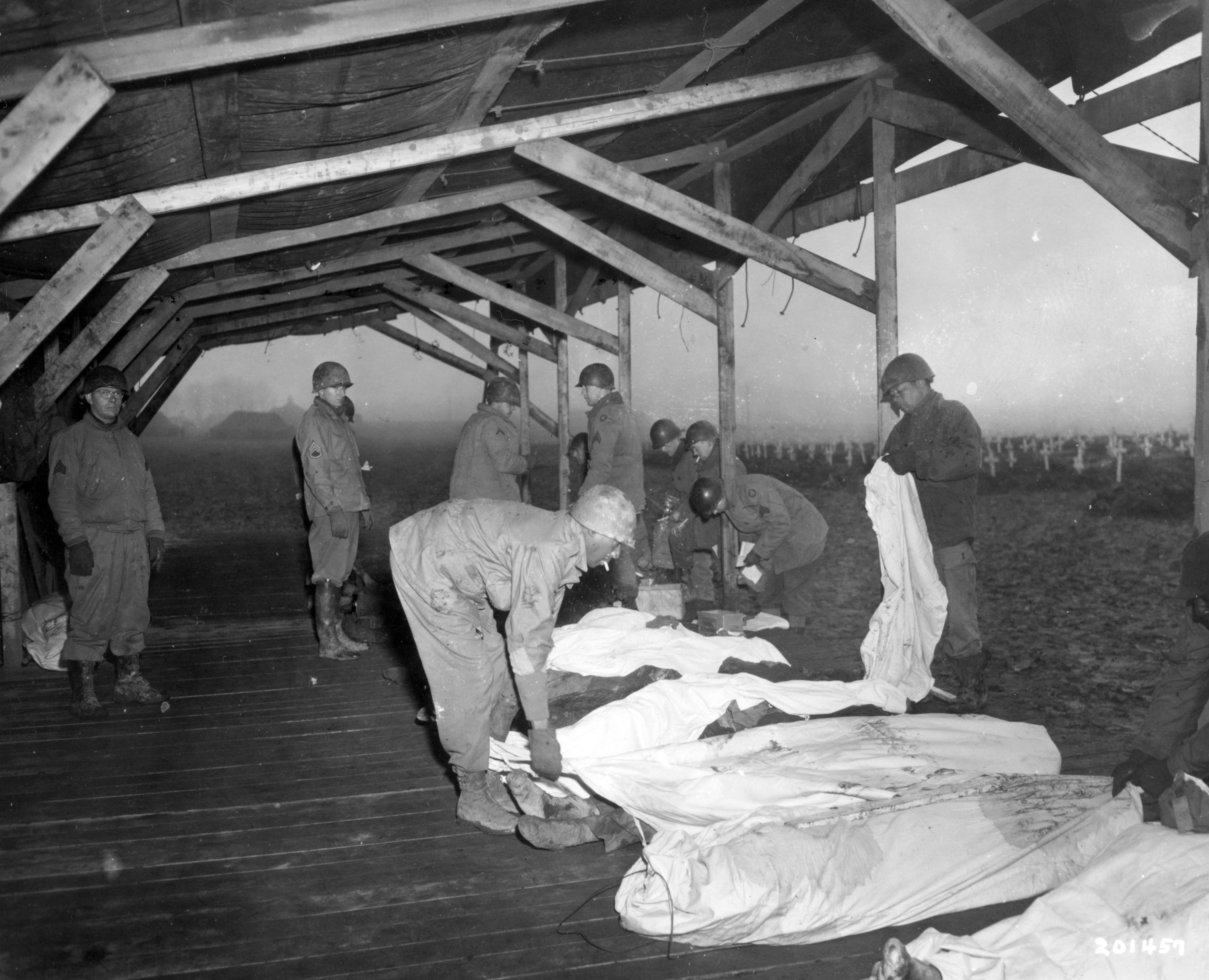 Historical image showing American casualties are wrapped in mattress covers for burial at U.S. Military Cemetery No. 1 in Foy, Belgium. of Black American soldiers during WWII