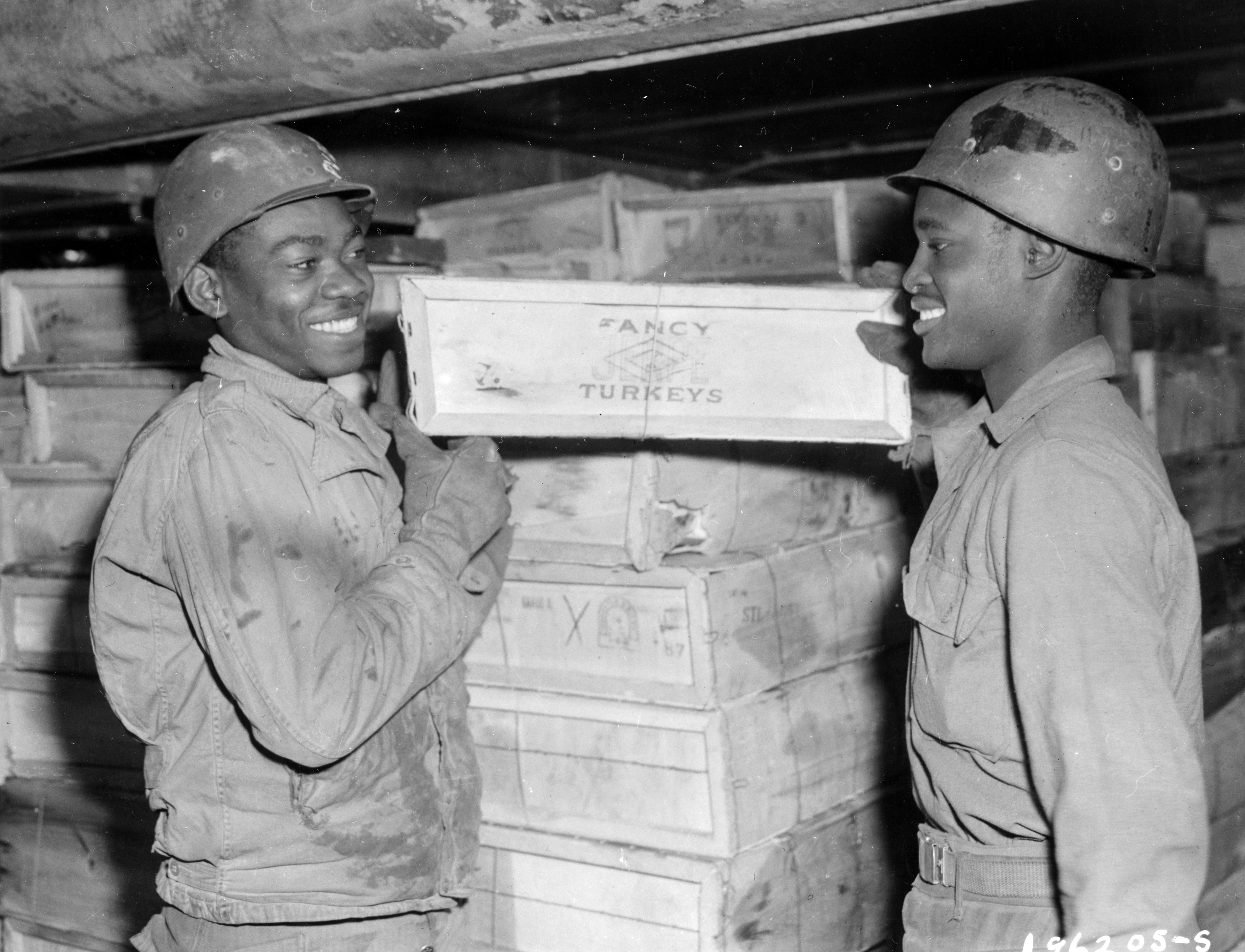 Historical image showing Members of a Port Battalion unload boxes of turkeys from liberty ships to trucks for transportation to all the fighting fronts for "Turkey Day" dinner. of Black American soldiers during WWII