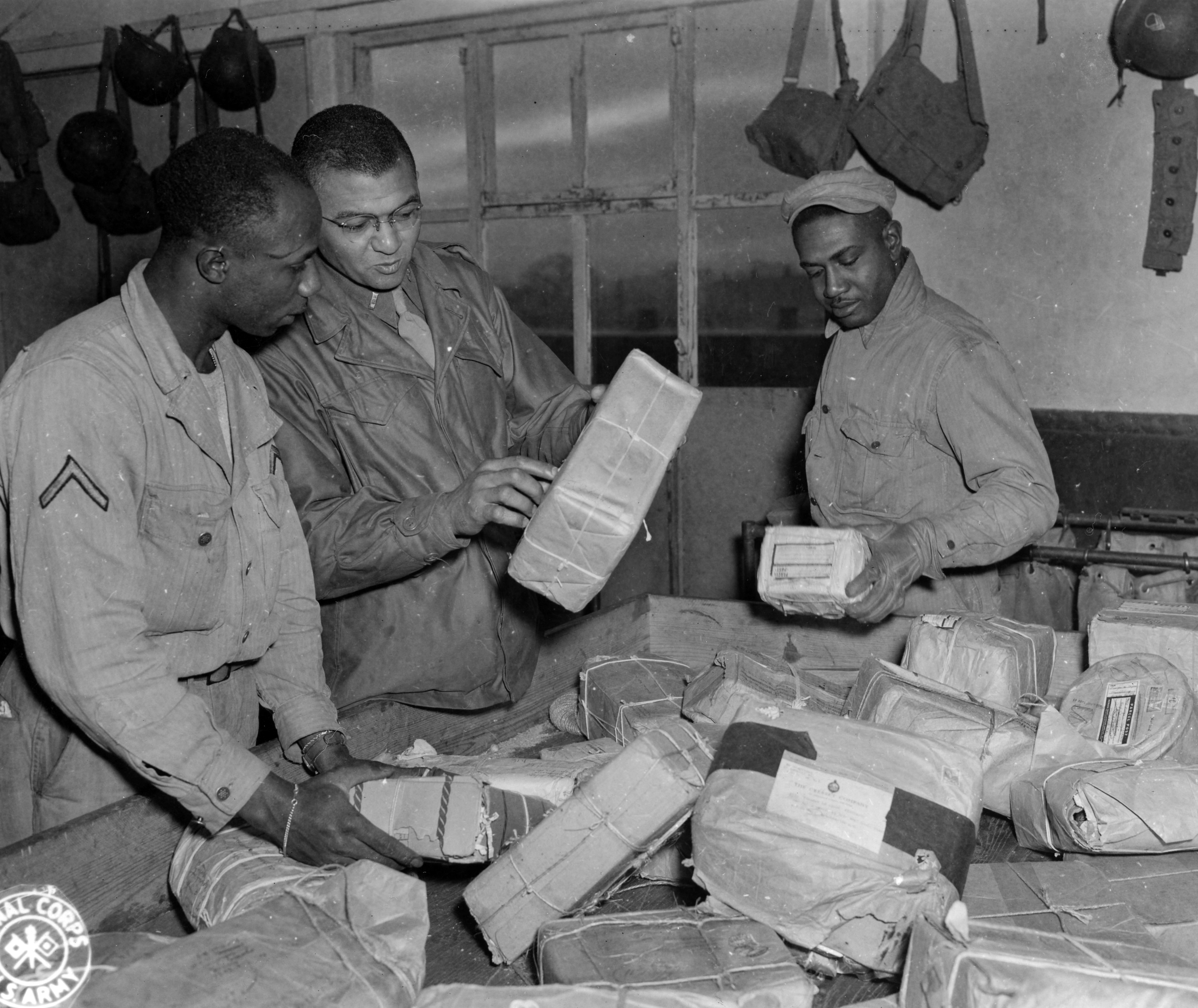 Historical image showing Personnel of the Postal Unit of a depot in England sort packages and mail. of Black American soldiers during WWII