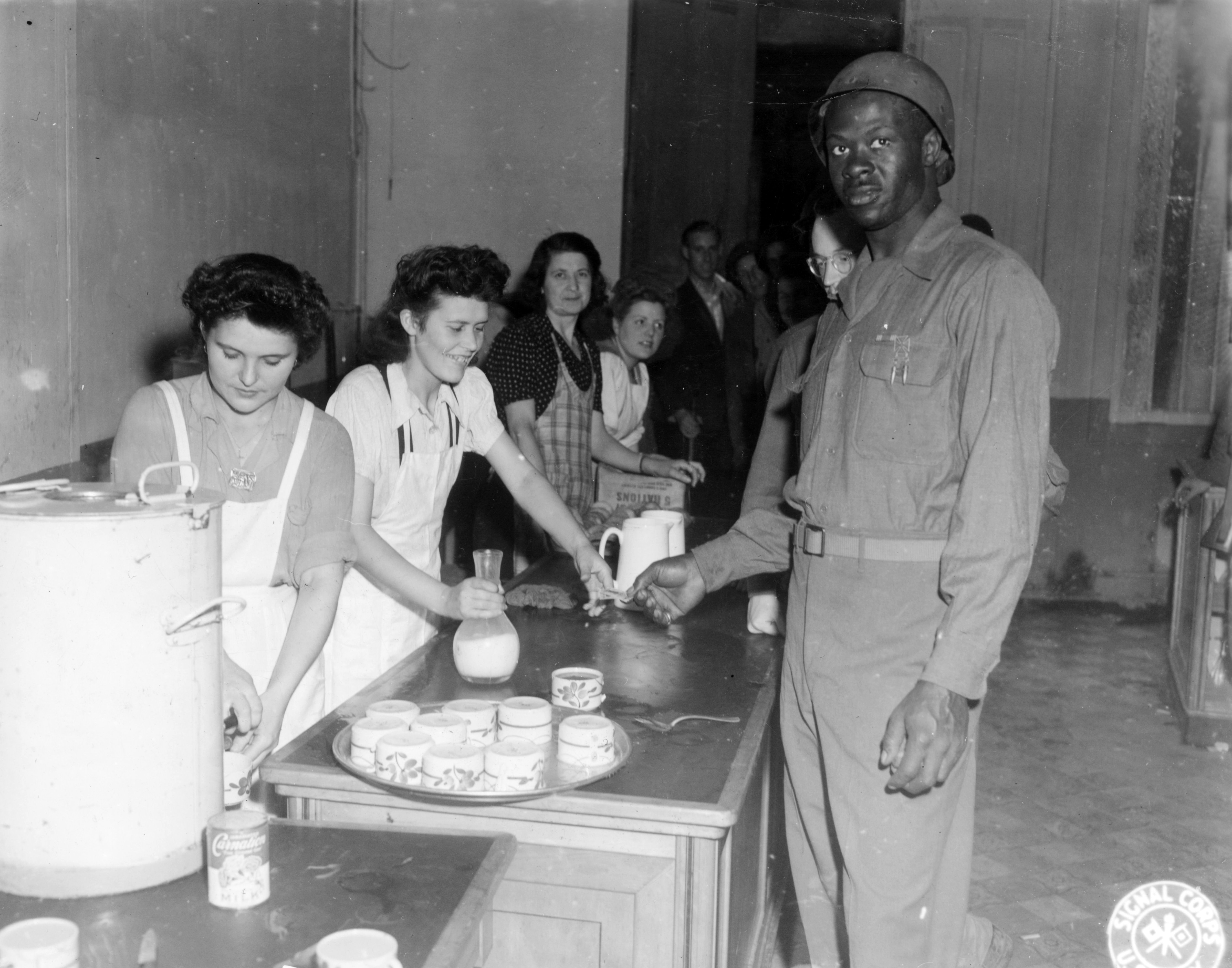 Historical image showing At the newly opened Red Cross club in Cherbourg, Corporal Charles C. Murphyel gets his share of Yankee doughnuts and coffee. of Black American soldiers during WWII