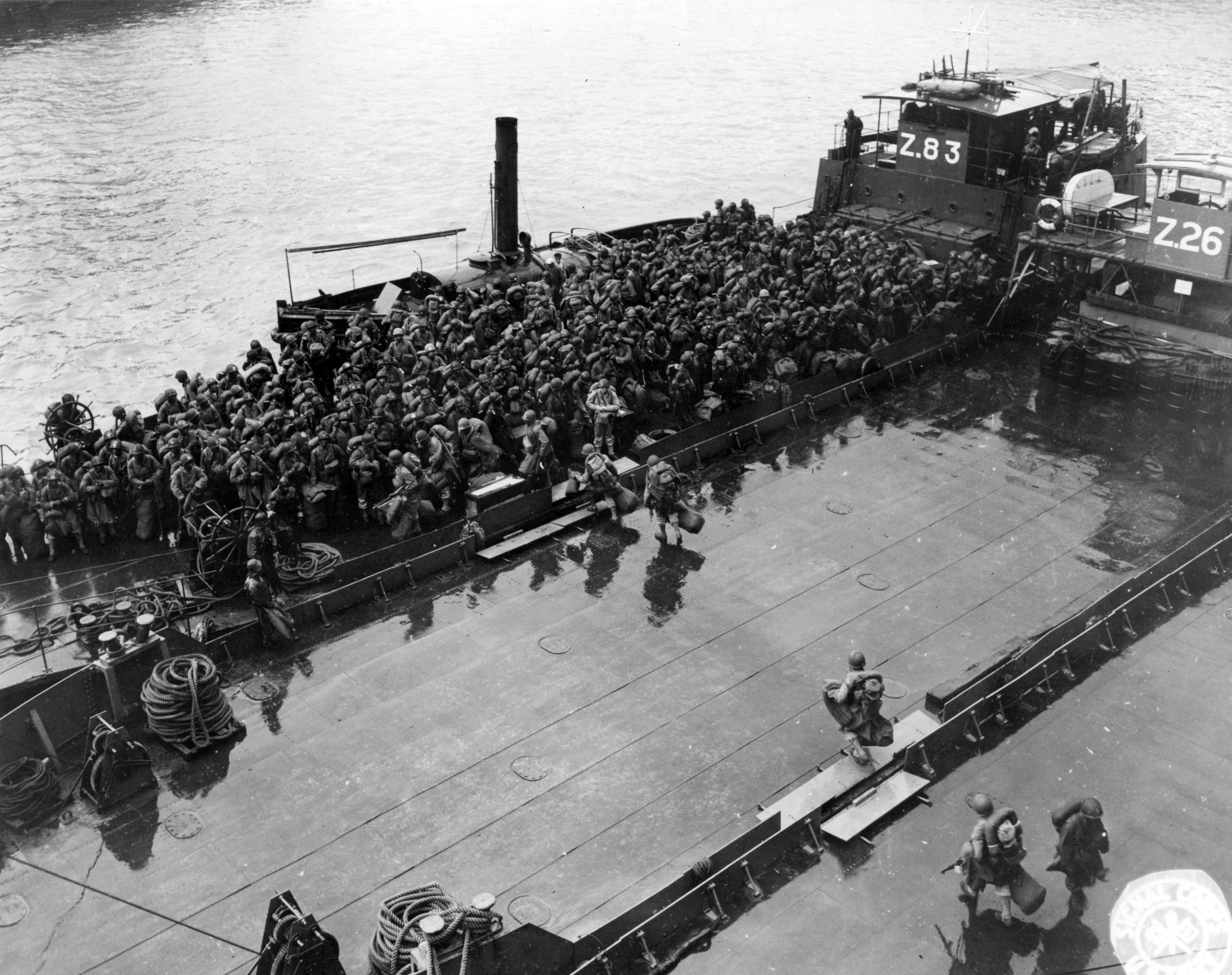 Historical image showing Heavily-laden American Black troops walk across the decks of British "Zed Lighters" to be carried ashore. of Black American soldiers during WWII